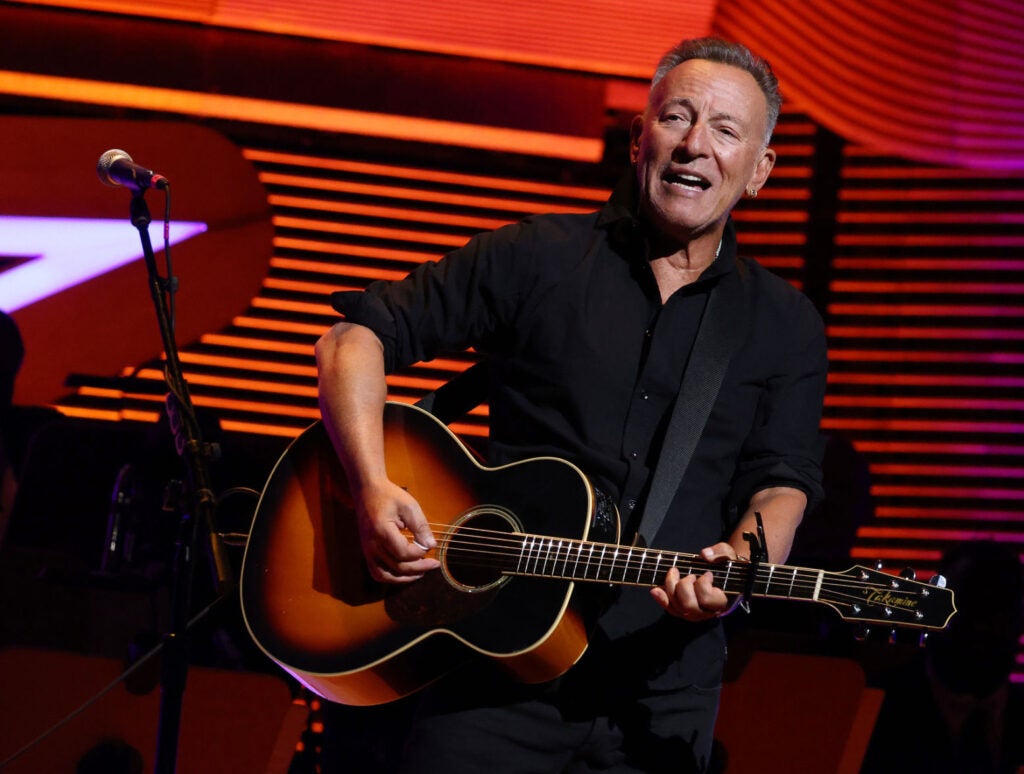 Zach Bryan's Brooklyn Concert- Bruce Springsteen wearing all black and playing guitar on stage. 